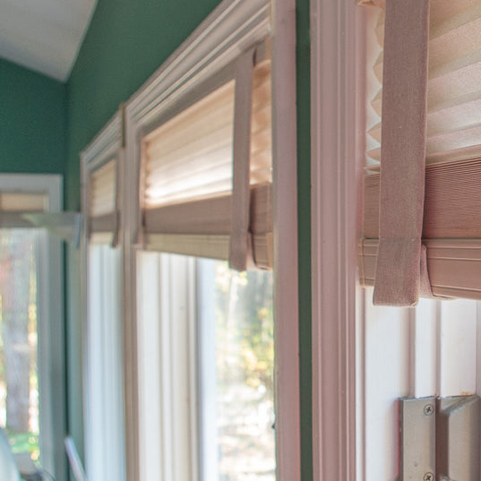 Side view of multiple windows with Lift Luxe Shade Straps in Linen Beige securing pleated window shades. The straps create a uniform, polished look, blending seamlessly with the soft natural light.