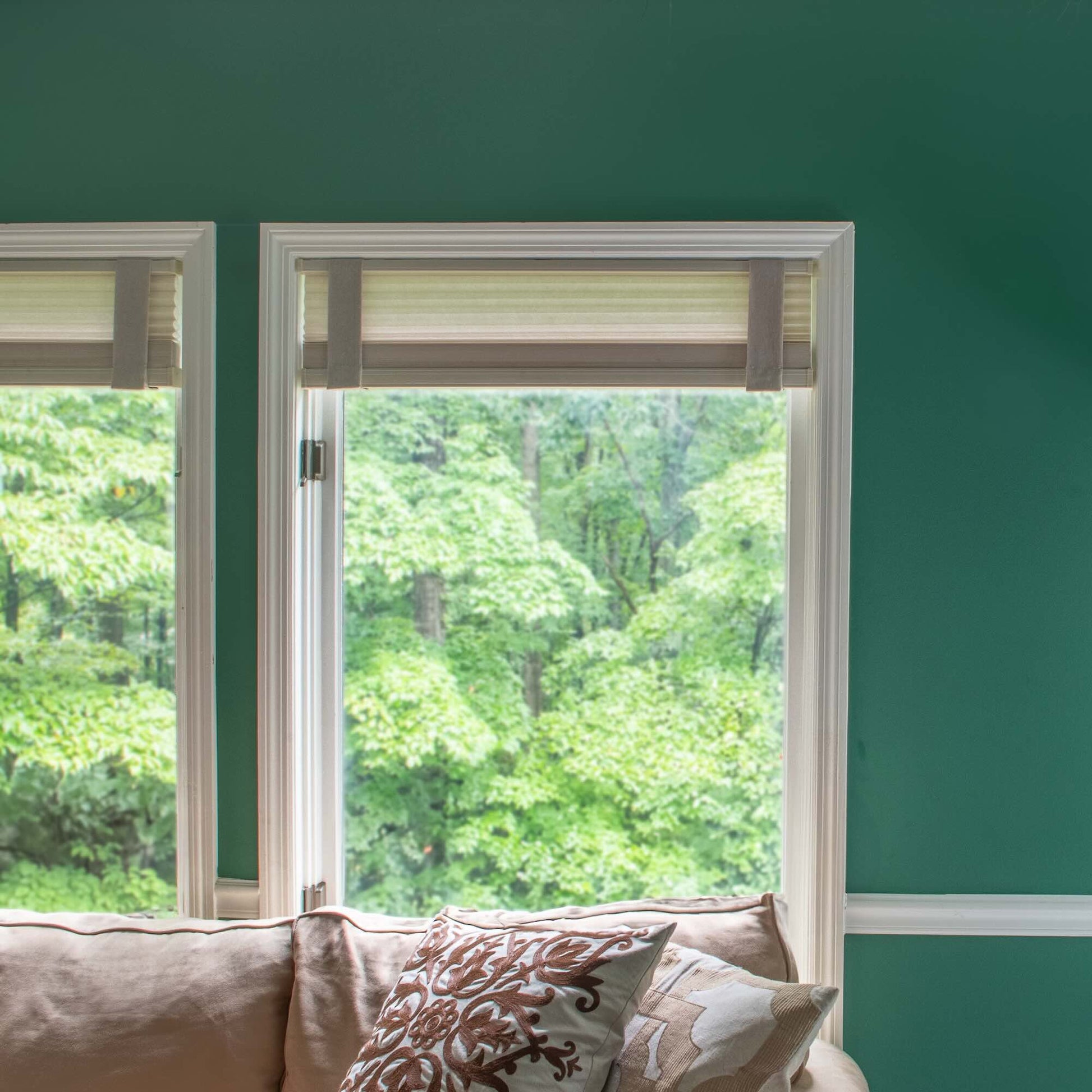 Living room window with Lift Luxe Shade Straps in Linen Beige. The window treatment is neatly aligned, with the shades held in place by the beige fabric straps, creating a polished, cohesive look against a bold green wall.