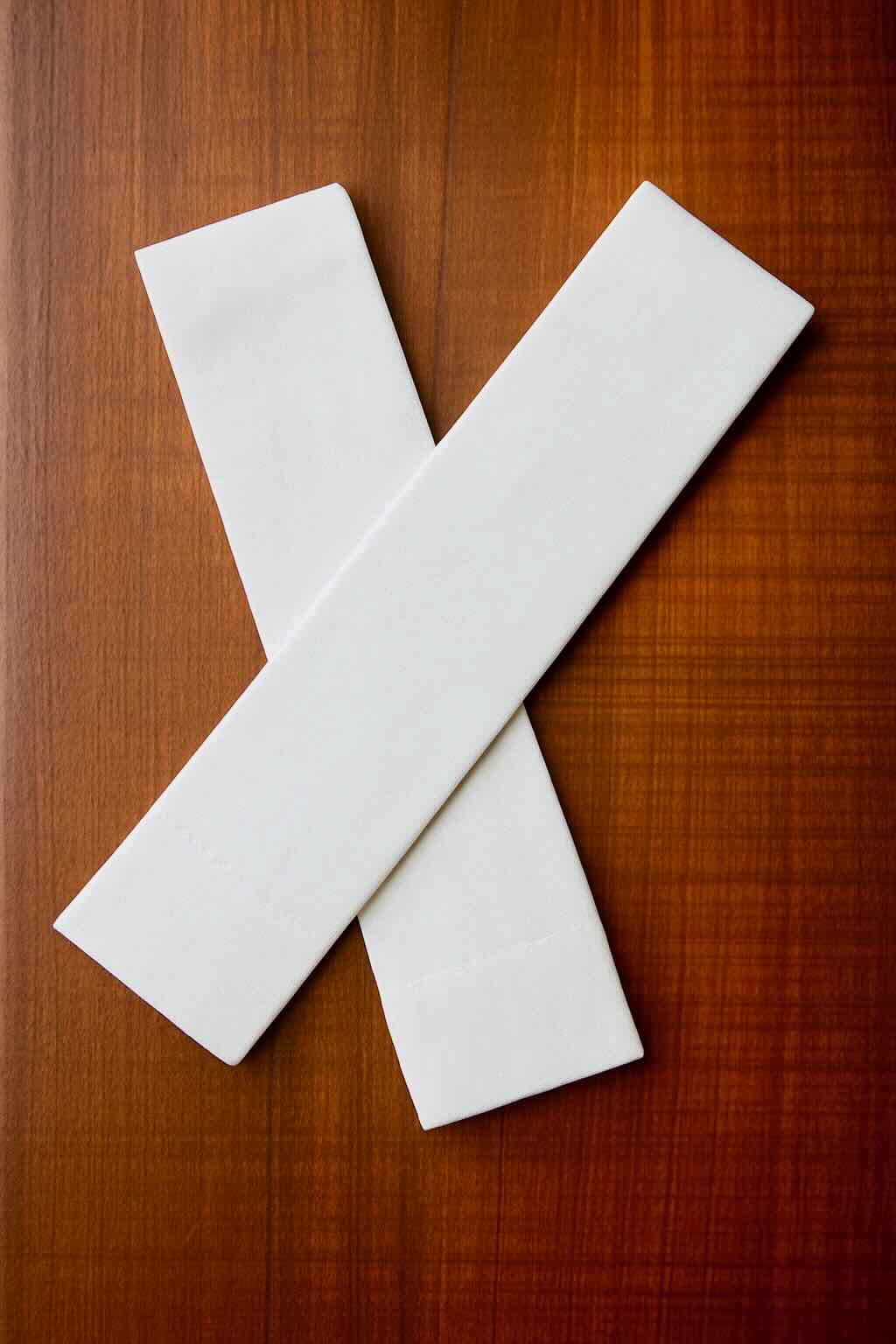 Two cotton white Lift Luxe Shade Straps crossed neatly on a polished wooden surface, showing the clean design and smooth woven texture of the fabric.