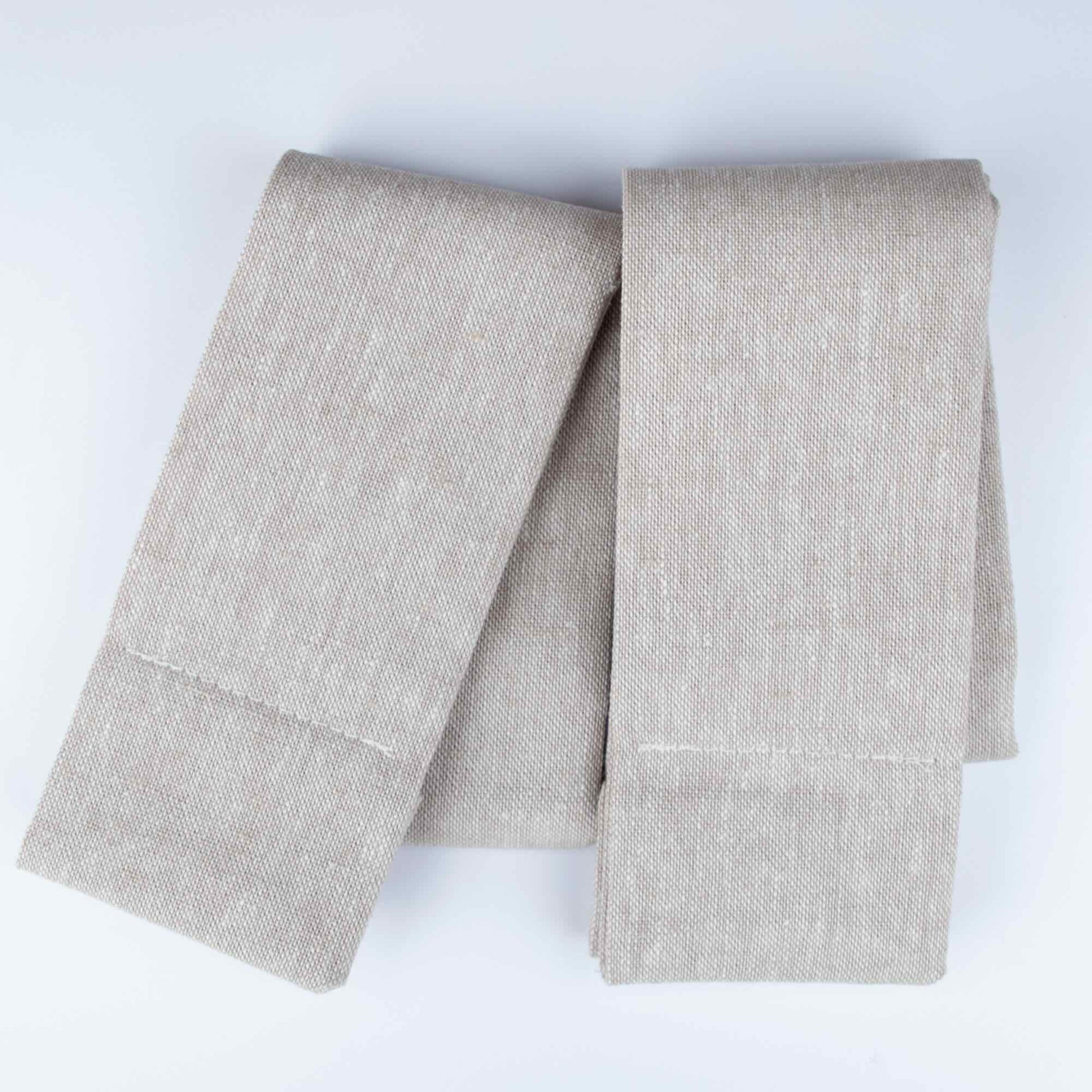A pair of natural linen Lift Luxe Shade Straps folded neatly against a light background, highlighting the fabric’s woven texture and simple design.
